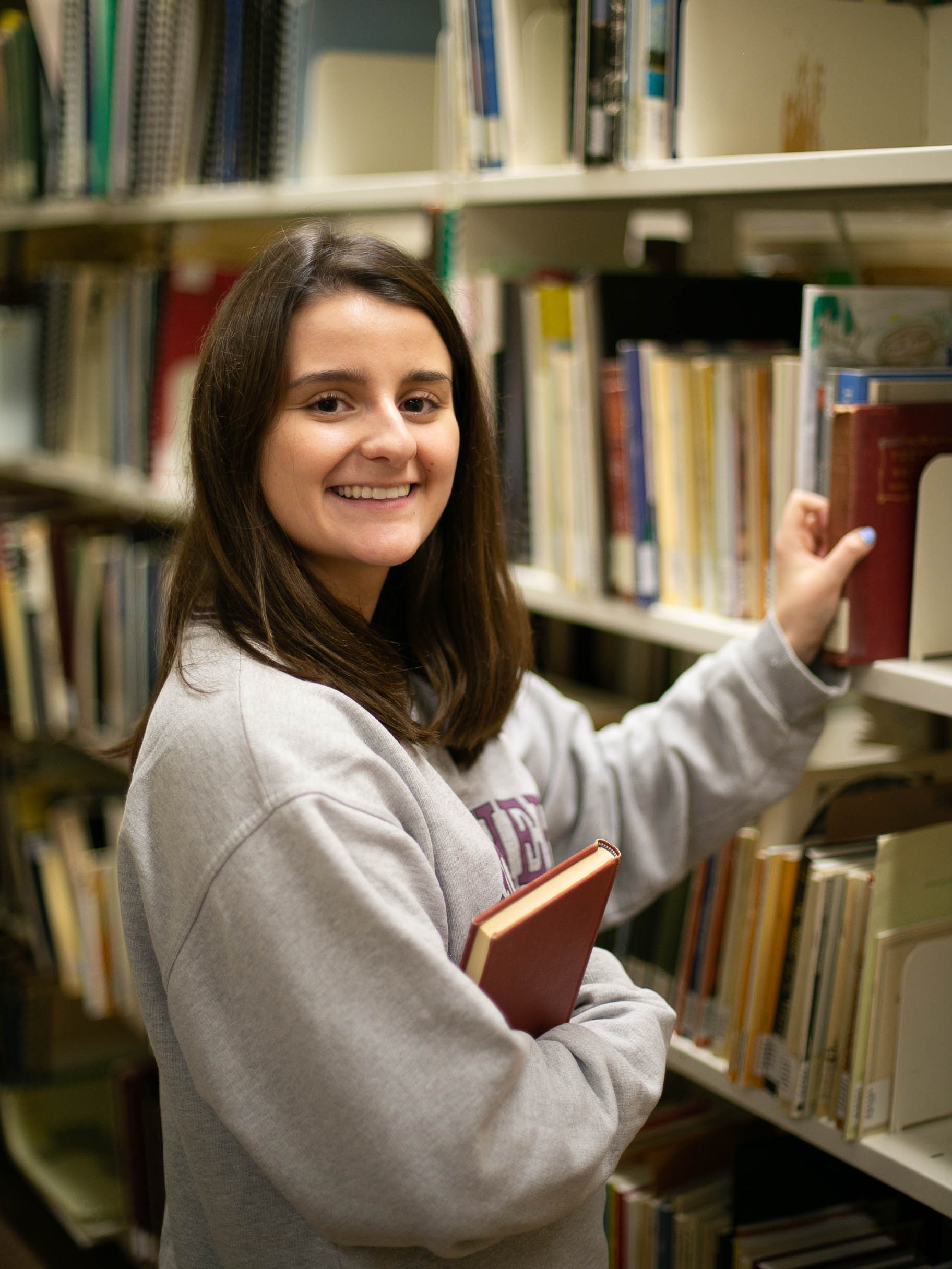 Maddie Savage is grabbing a book from a shelf while in the library