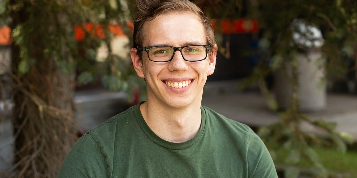 A young student is smiling while sitting on a chair outside