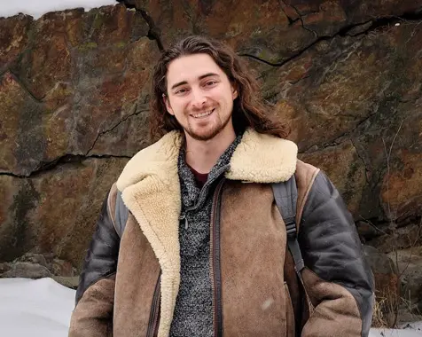 Devon Patterson stands outside in front of a wall of rocks, smiling. 