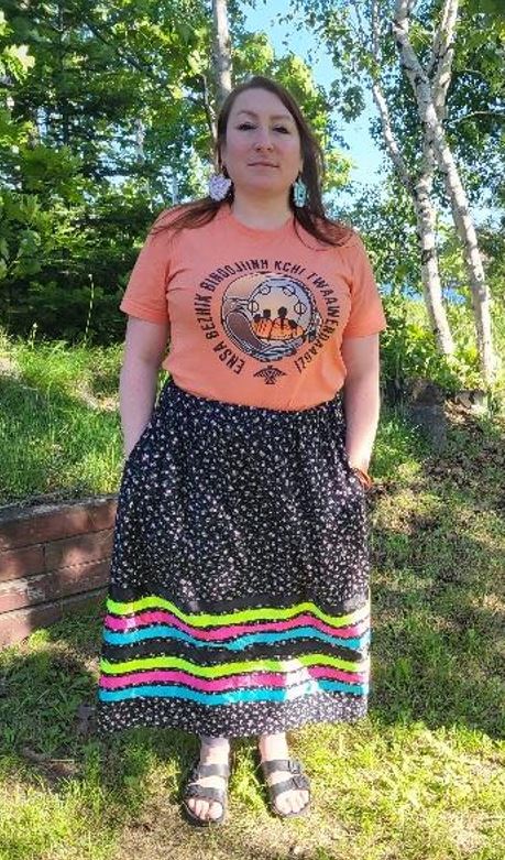Sheri Cecchetto, Field Coordinator, Indigenous woman wearing a Ribbon skirt with sun and trees in the background.