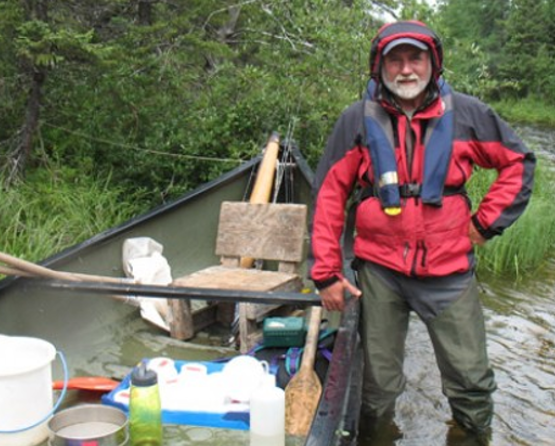 Bill Keller smiling next to a canoe