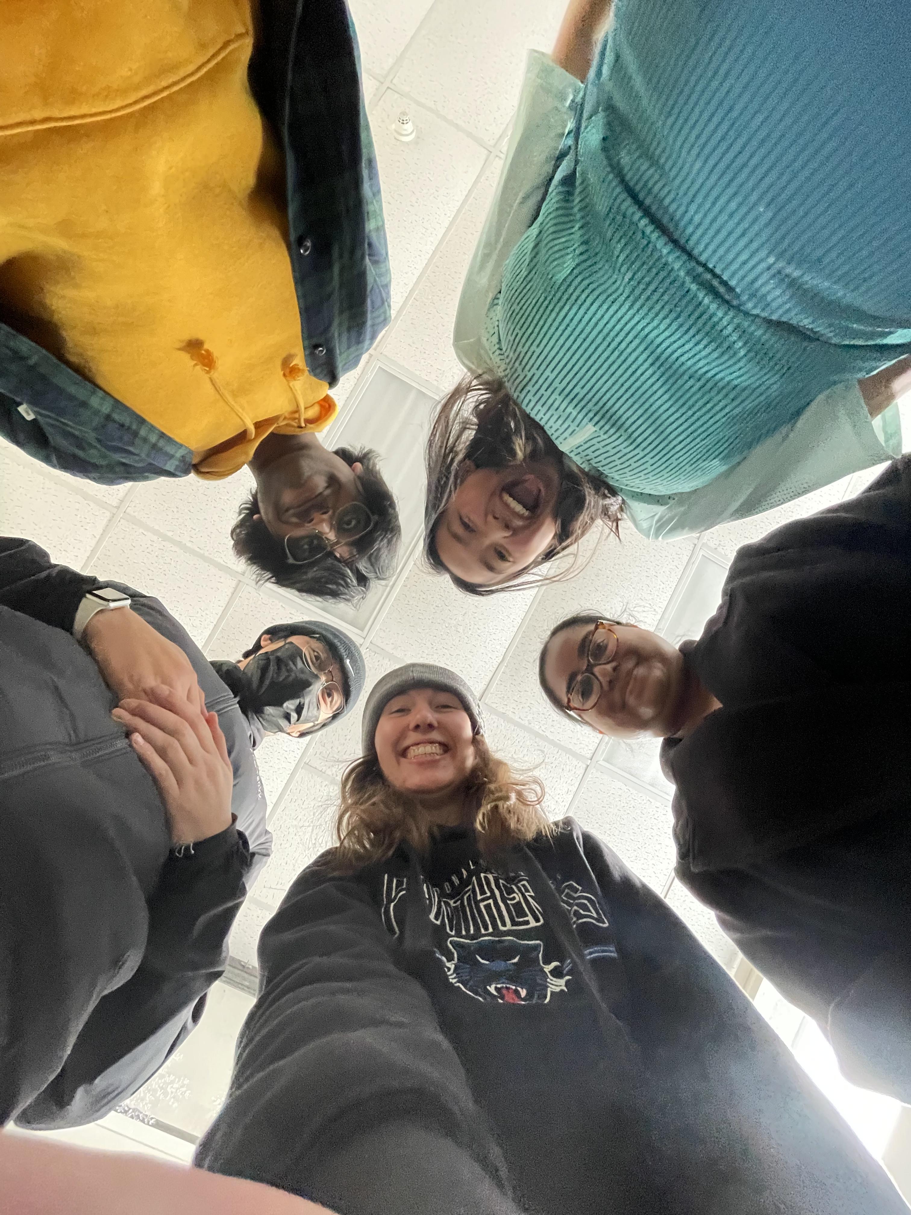 students standing in a circle looking down at the camera