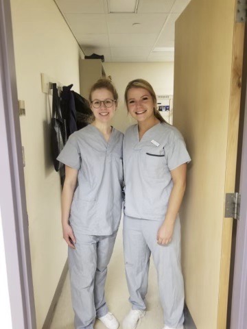 Alexie-(right)-stands-beside-friend-and-student-peer,-Emilie-Plach-(left),-in-a-clinical-setting.