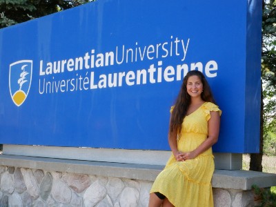 Sarah de Blois sitting in front of the Laurentian entrance sign 