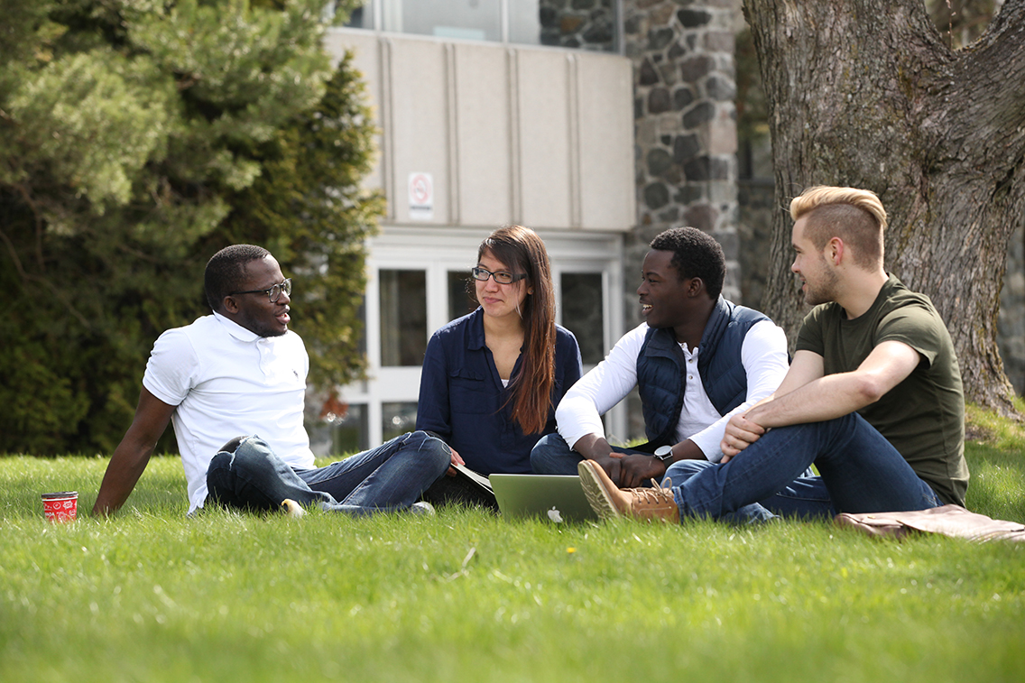 four students sitting outside in the grass
