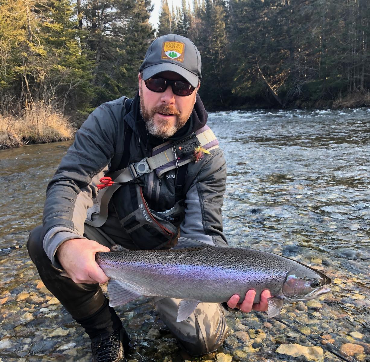 Lee Haslam holding a rainbow trout on the edge of a river