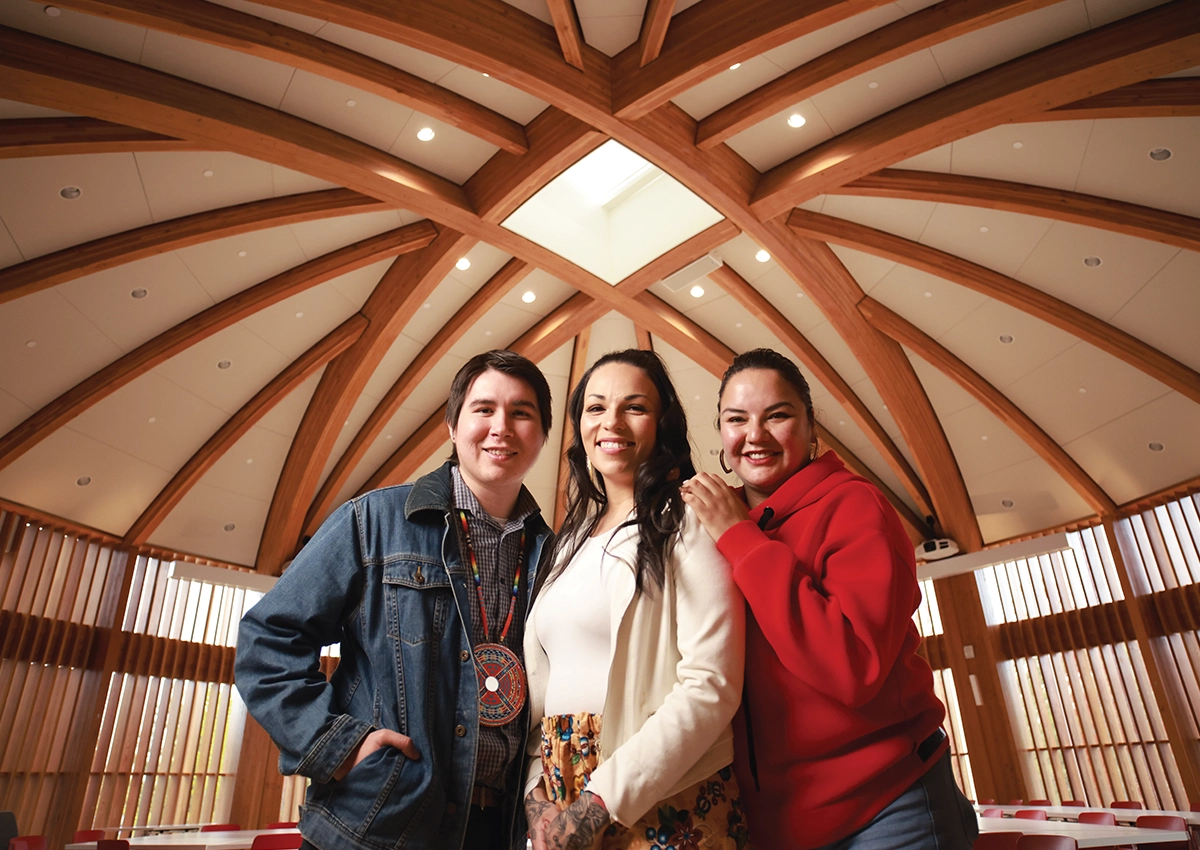 Three Indigenous Laurentian University students standing and smiling in the Indigenous Sharing and Learning Centre.