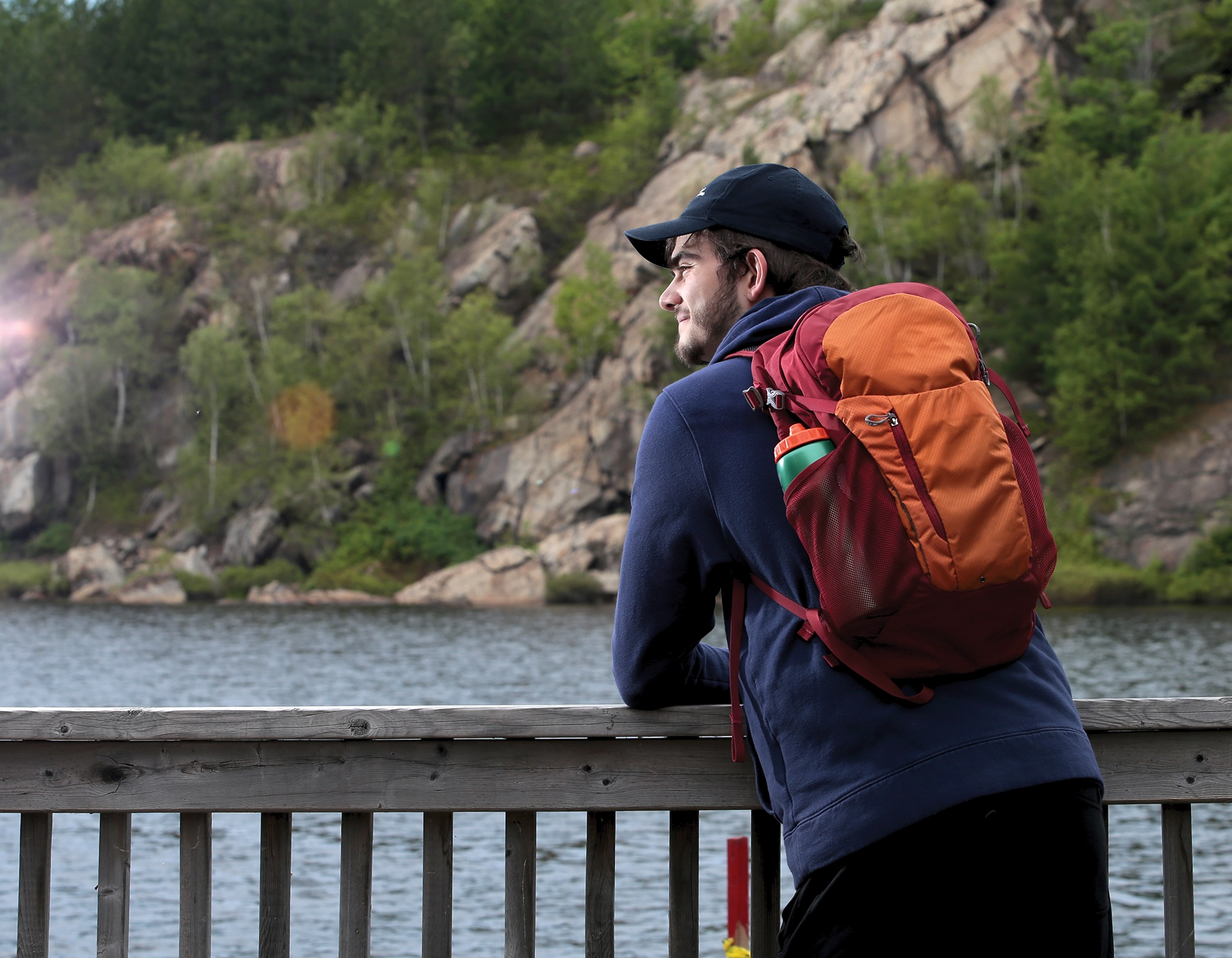 A Laurentian University student on campus and leaning against a wooden railing that overlooks a lake.