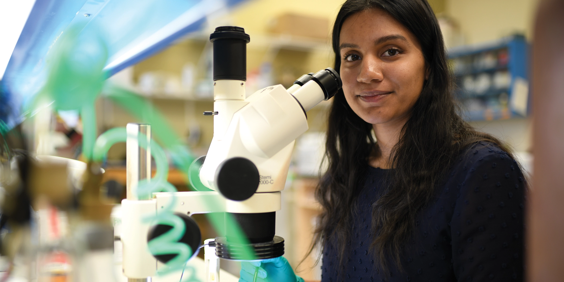 Student using a microscope, smiling at camera.