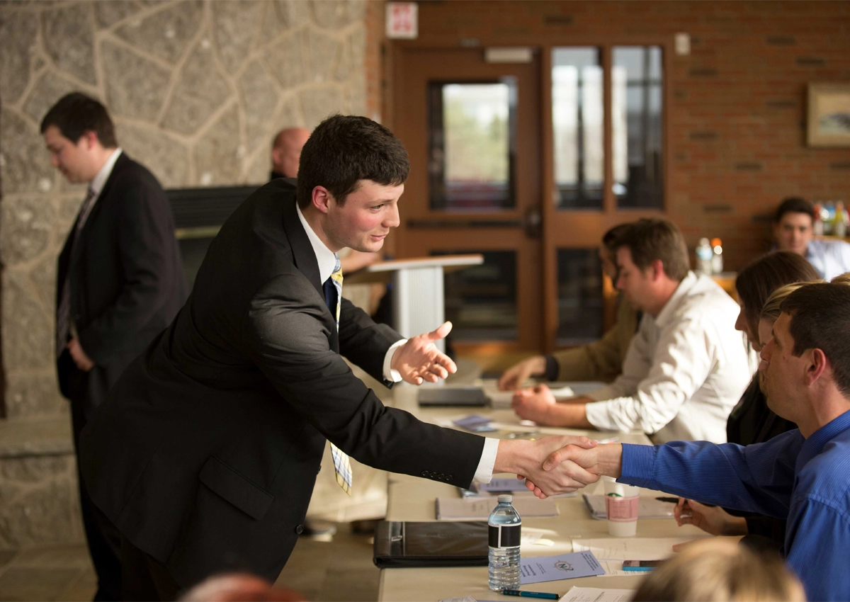 A student wearing a suit shaking hands with a business professional in the Brenda Wallace Reading Room.