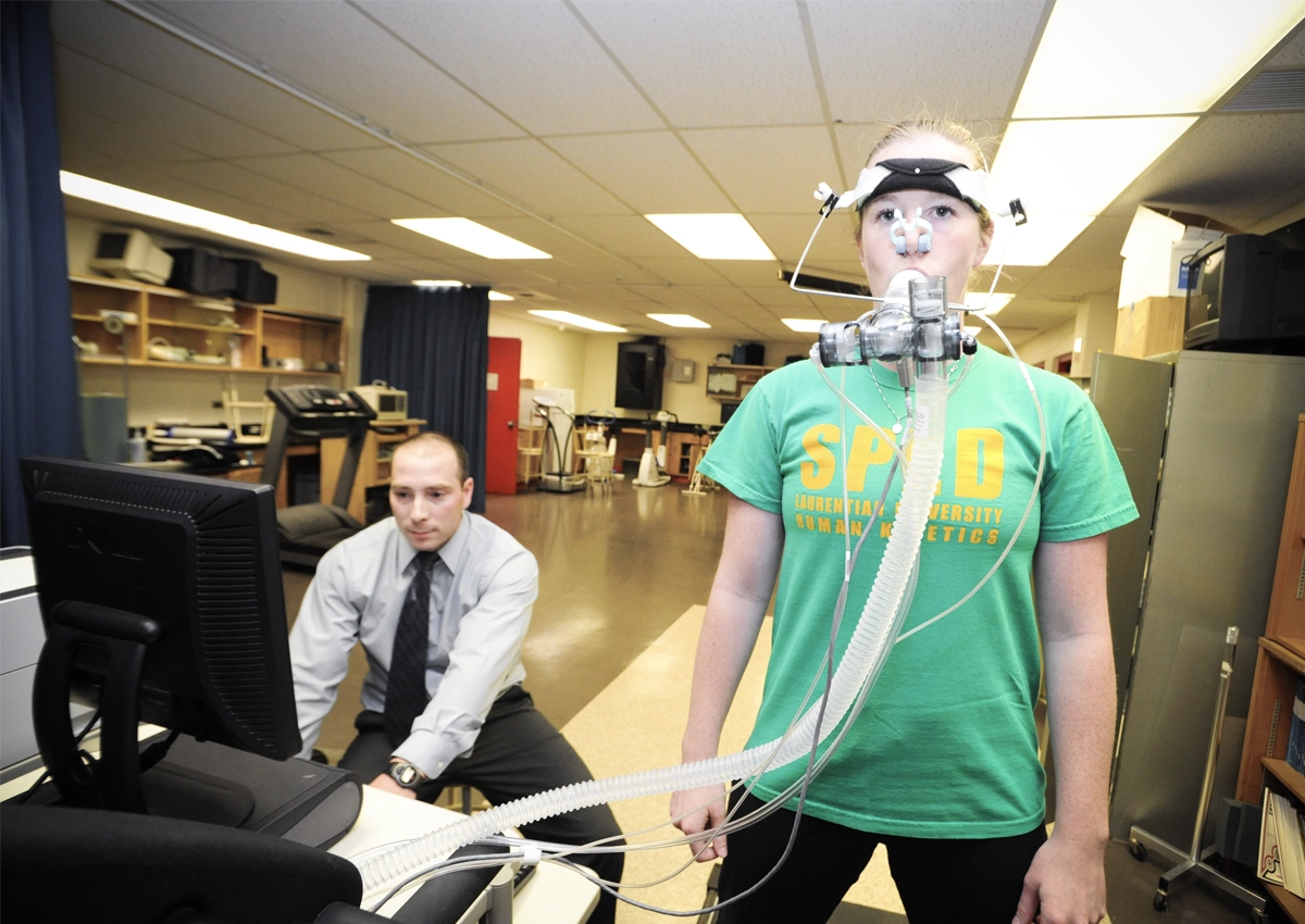 A Human Kinetics student using a breathing monitoring device while her professor monitors the data collected on a computer.