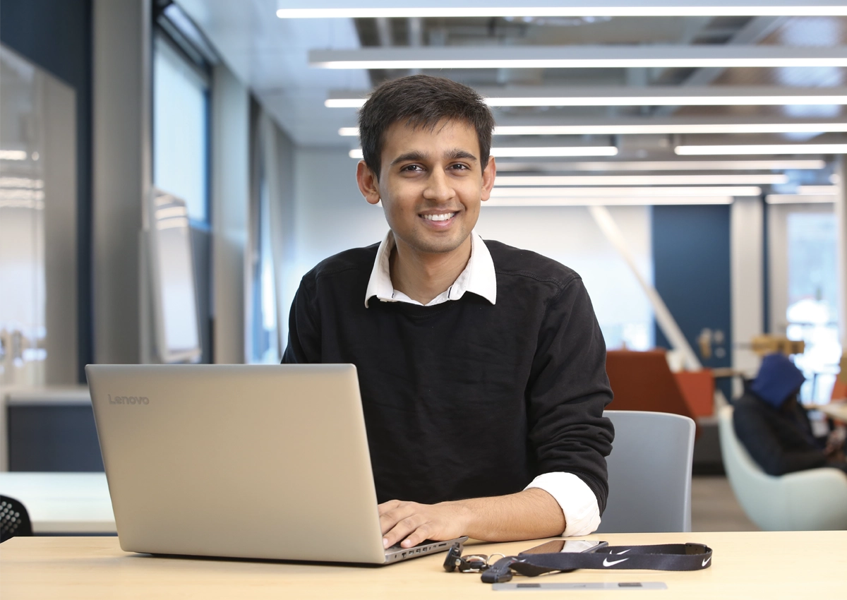 A Laurentian University student using a laptop, smiling at the camera.