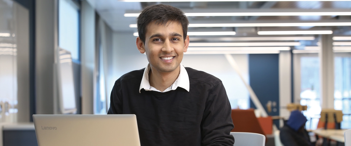 A Laurentian University student using a laptop, smiling at the camera.
