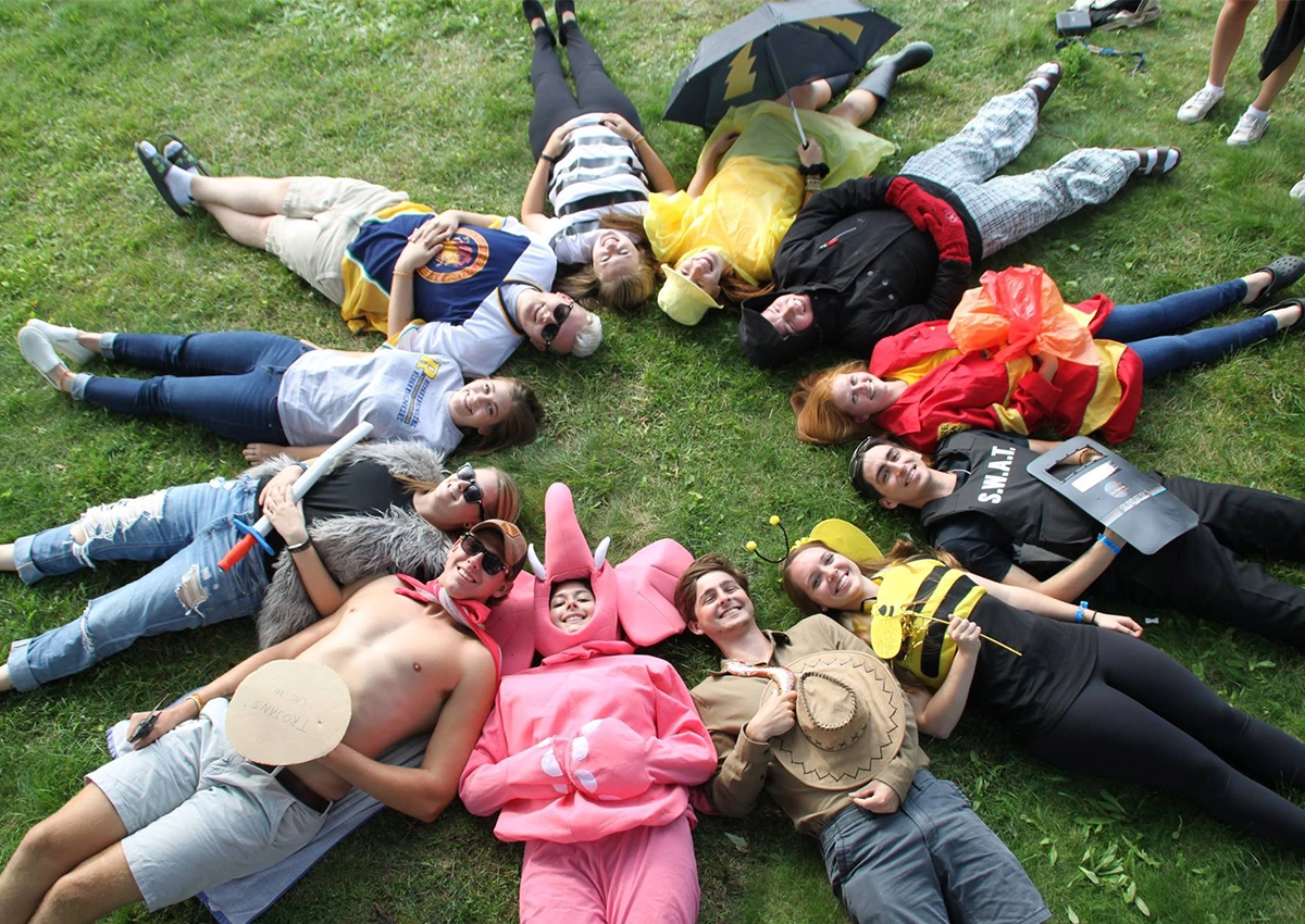 Residence employees in costumes sitting in a circle together on the grass.