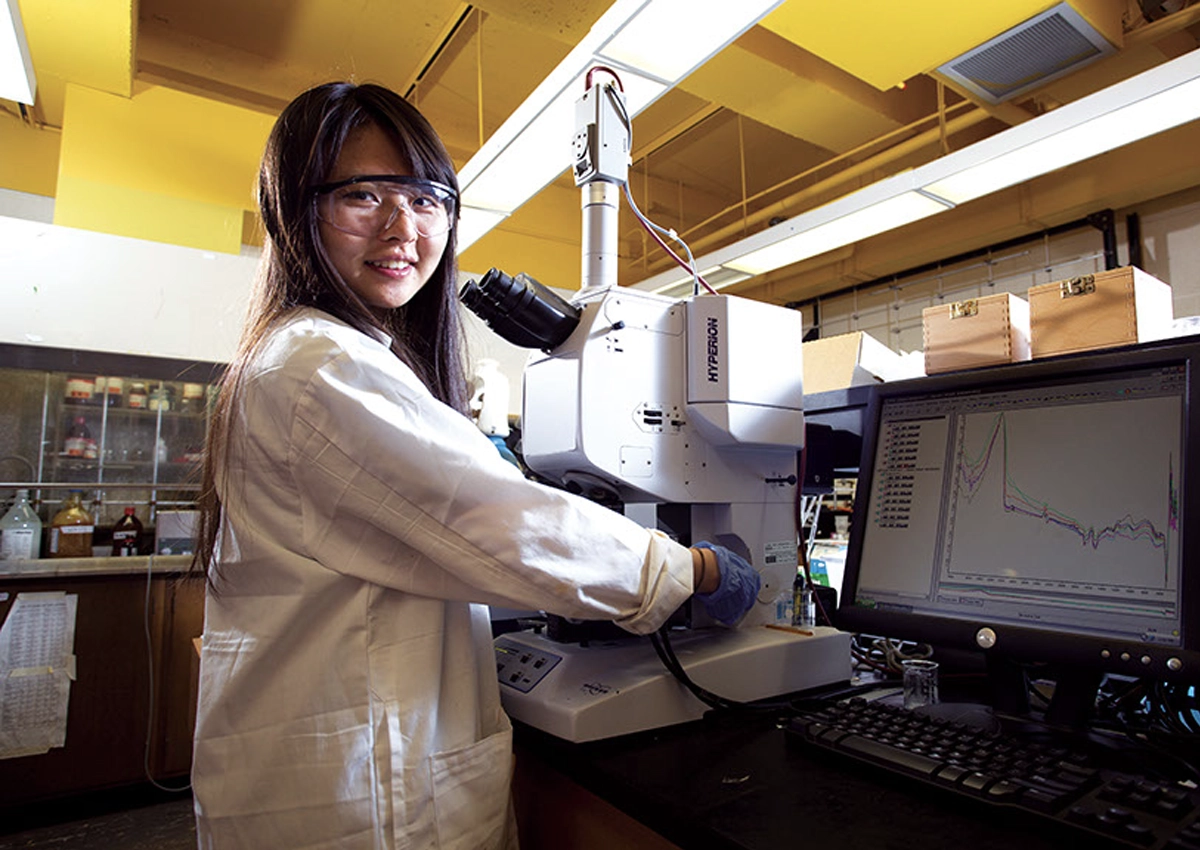 Young woman wearing a lab coat, working with a microscope.