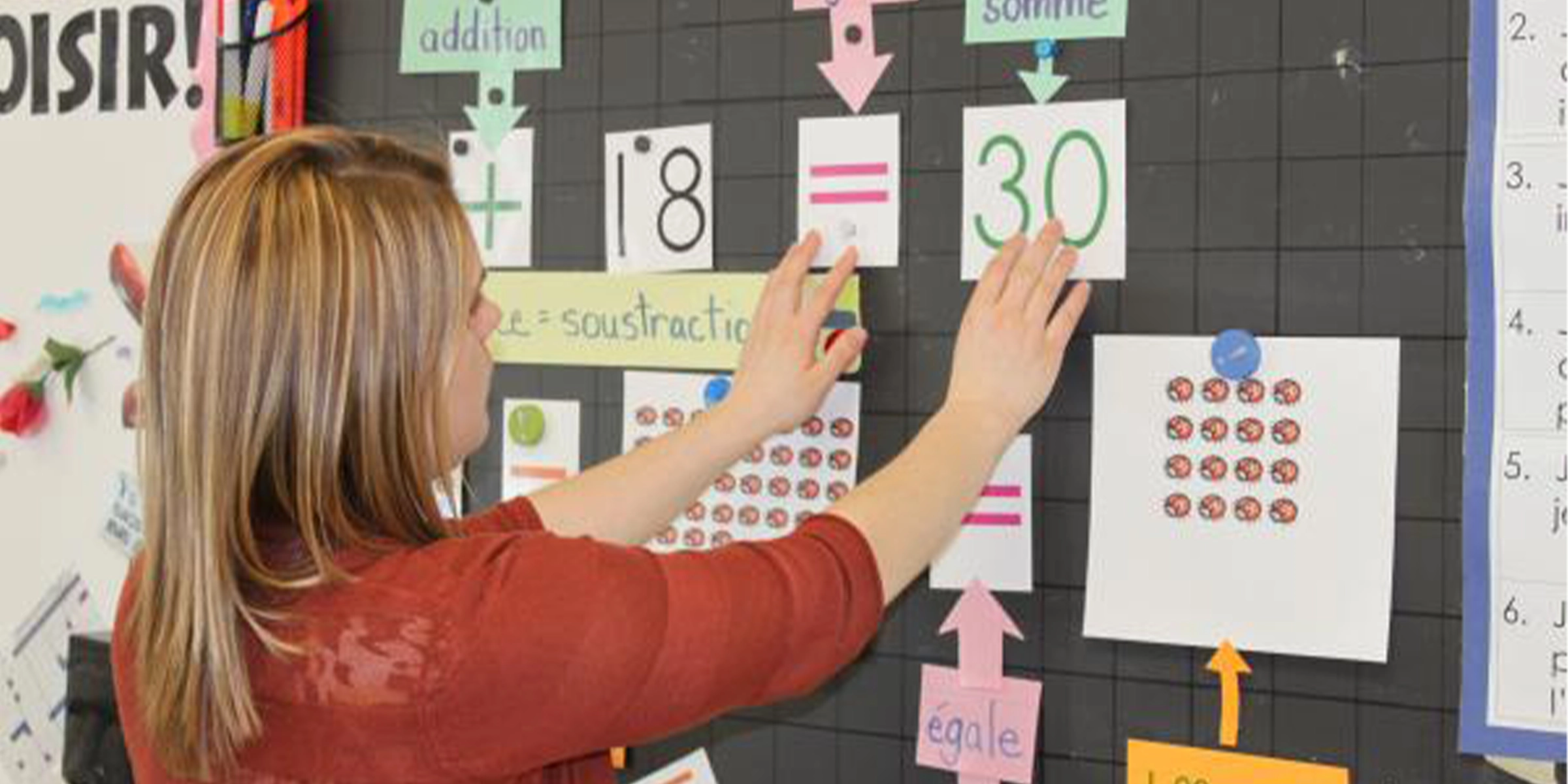 A teacher rearranges a bulletin board in her classroom.