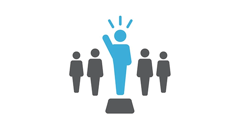A person standing on a podium with their hand raised, with other people standing quietly behind them.
