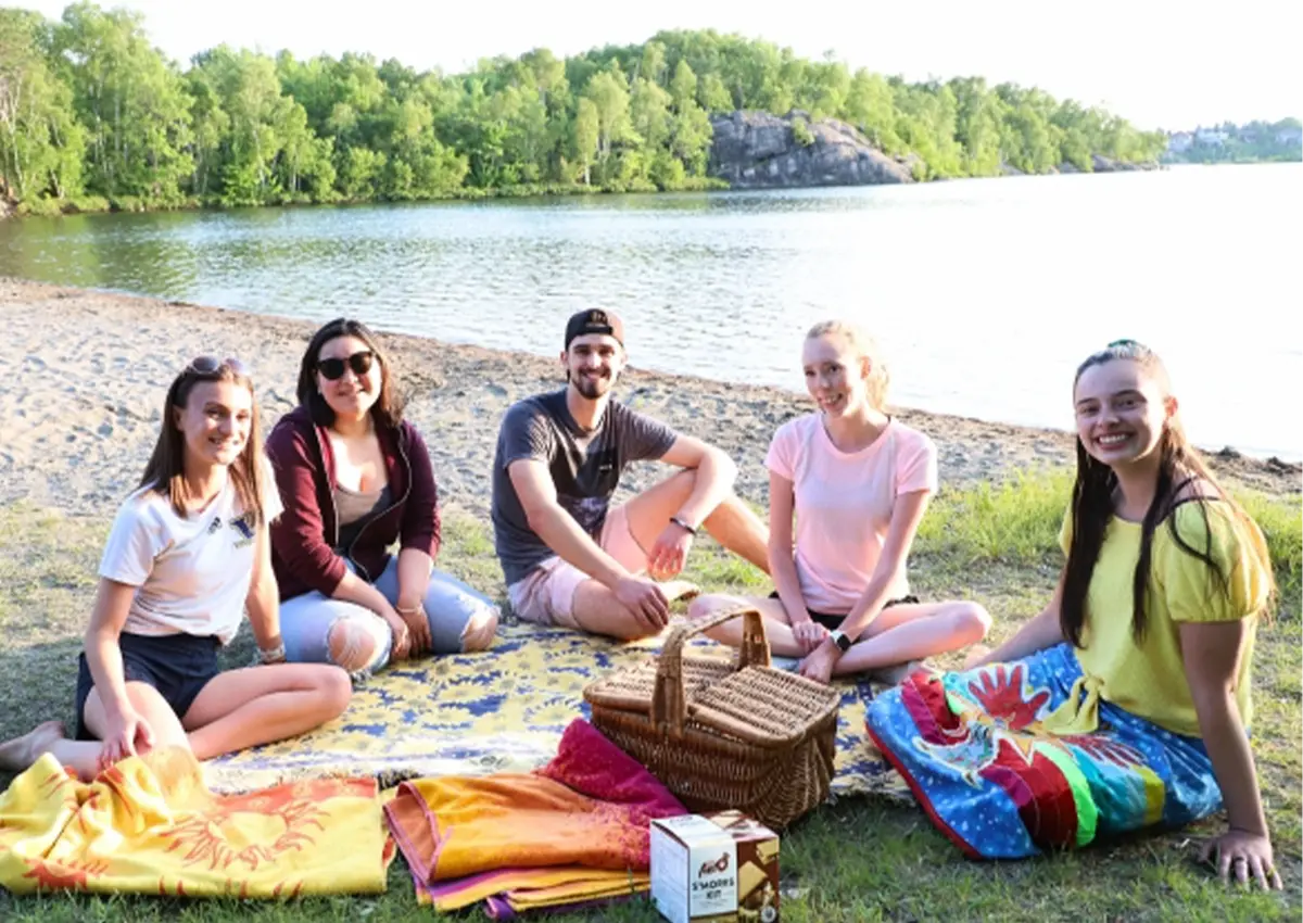 A group of Laurentian University students sitting by Nepahwin Lake at Laurentian Beach.