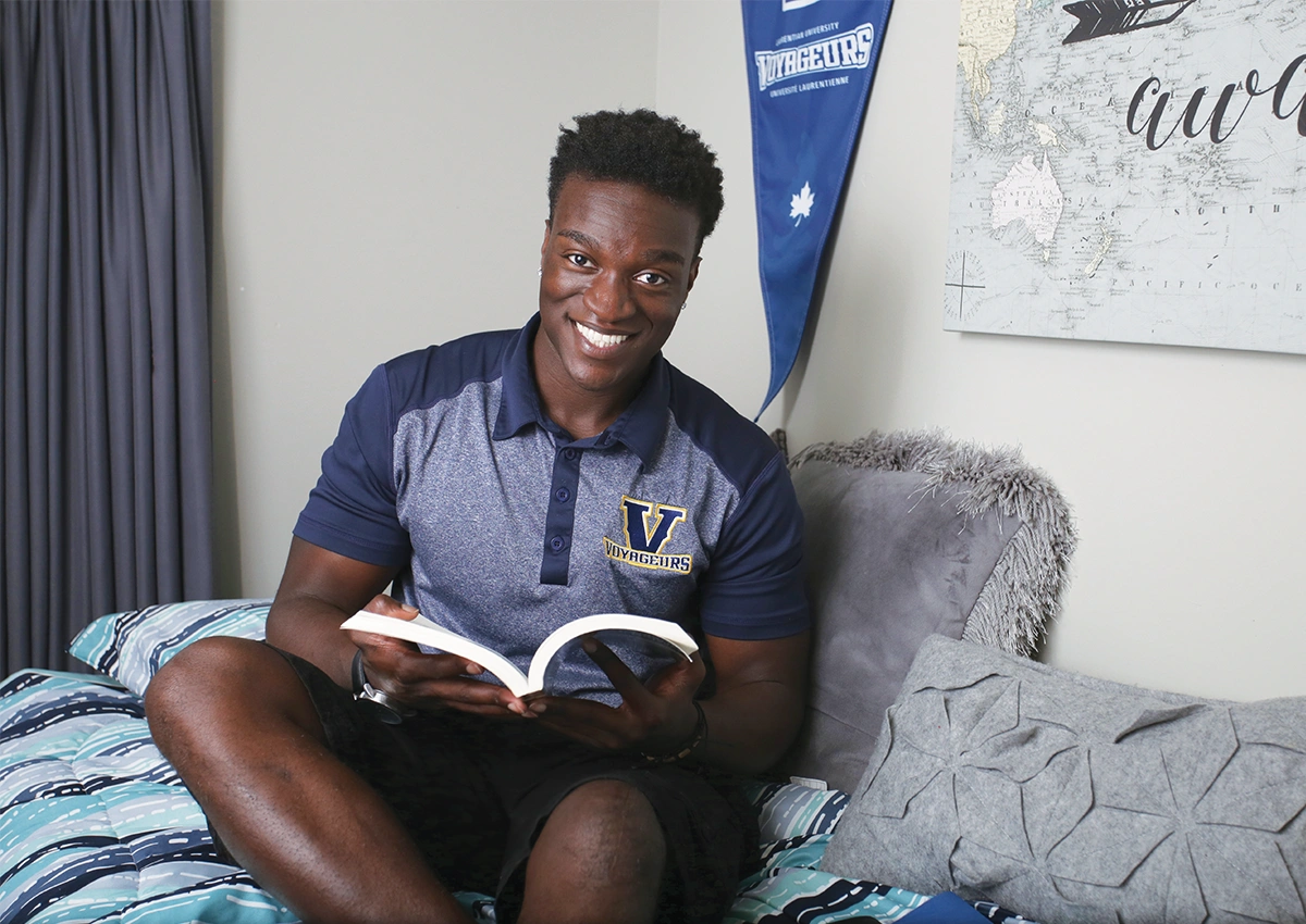 A Laurentian University student reading a book in his residence room.