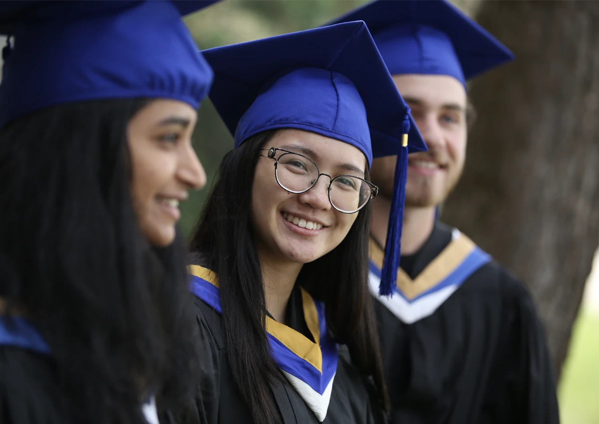 Three students wearing black, blue and yellow convocation attire, smiling.