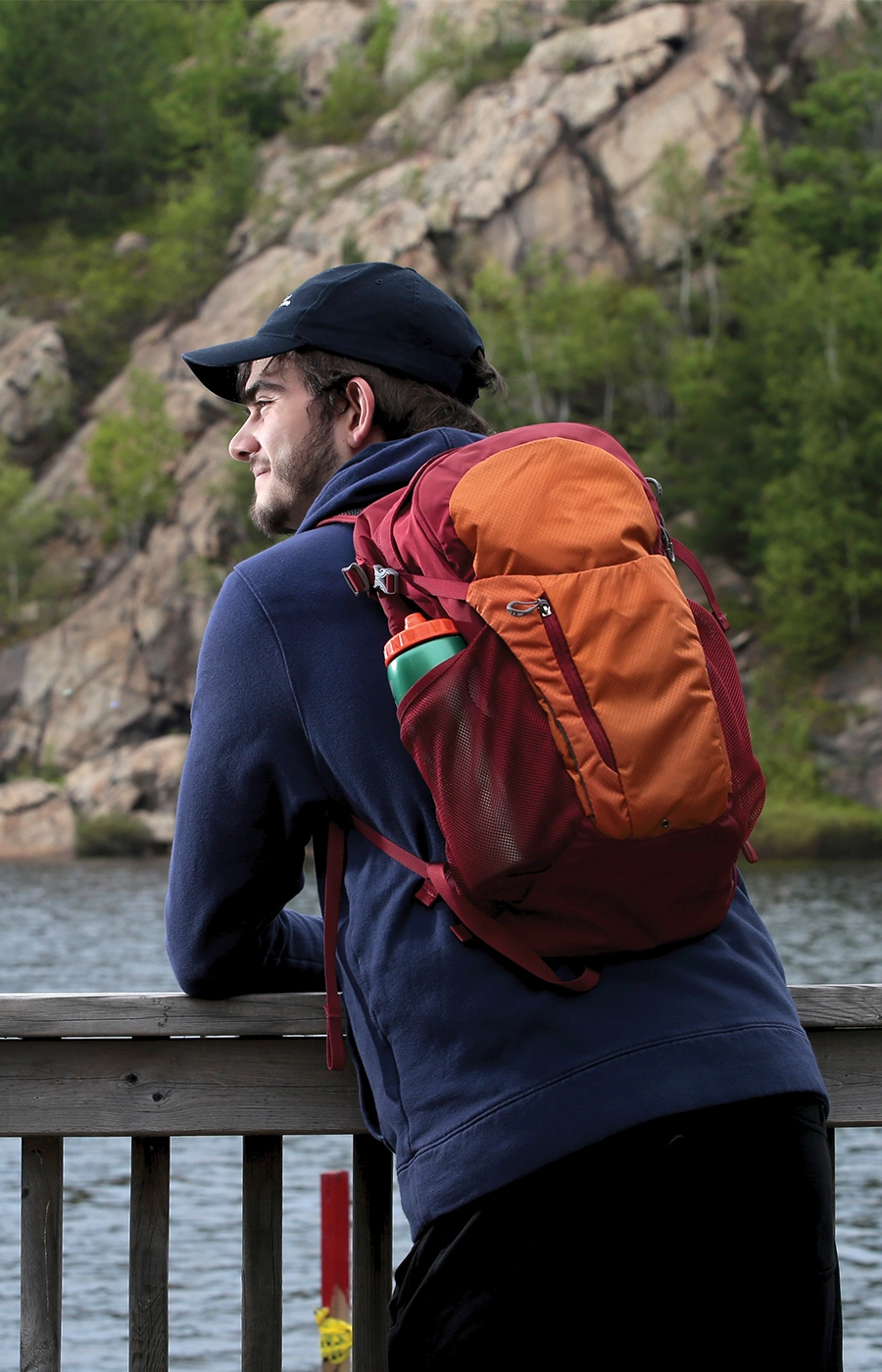 A Laurentian University student leaning on a railing in front of a lake and rocks.