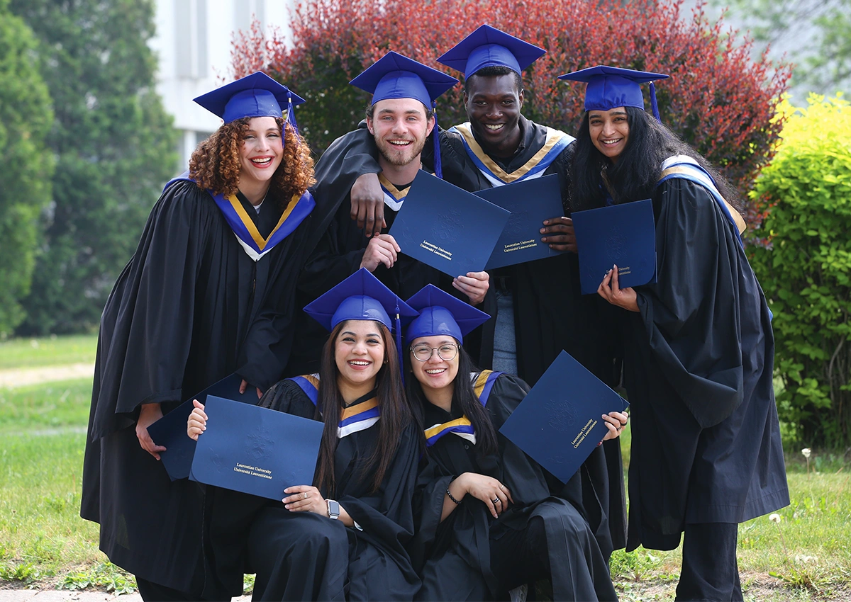 Laurentian University graduates posing outside with their degrees.