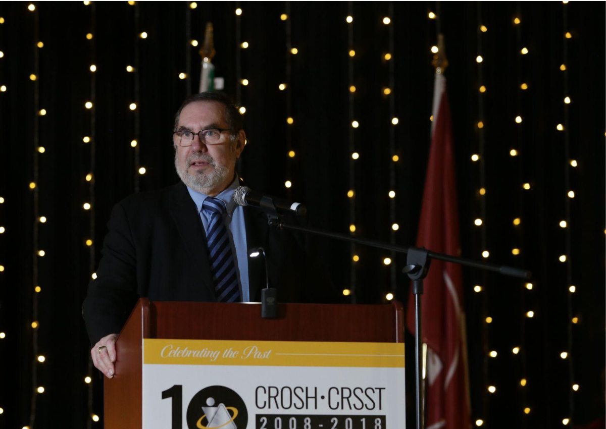 Dr. Leo Gerard speaking at a podium during a presentation for CROSH, addressing an audience.