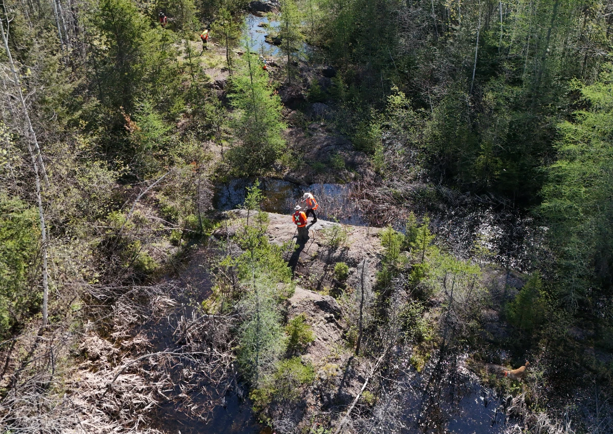 A group of students with a prof doing research on a large rock in the forest.