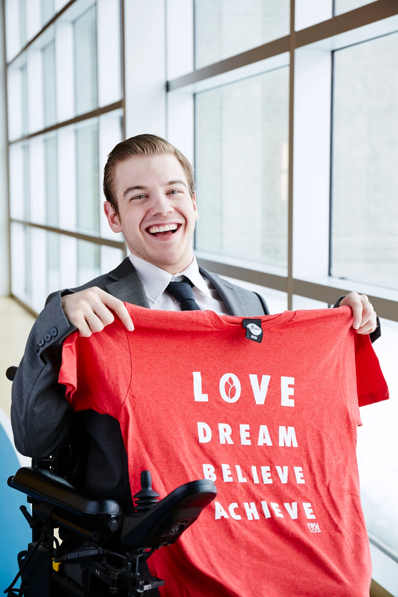 Ryan Benoit proudly smiles with a red t-shirt from his brand, The Positive Inception.