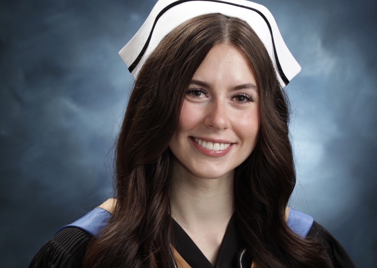 A formal graduation portrait of nursing graduate Alex Kowalski. She is smiling warmly while wearing a black academic gown, a traditional white nurse's cap, and a stethoscope around her neck, holding a bouquet of red roses.