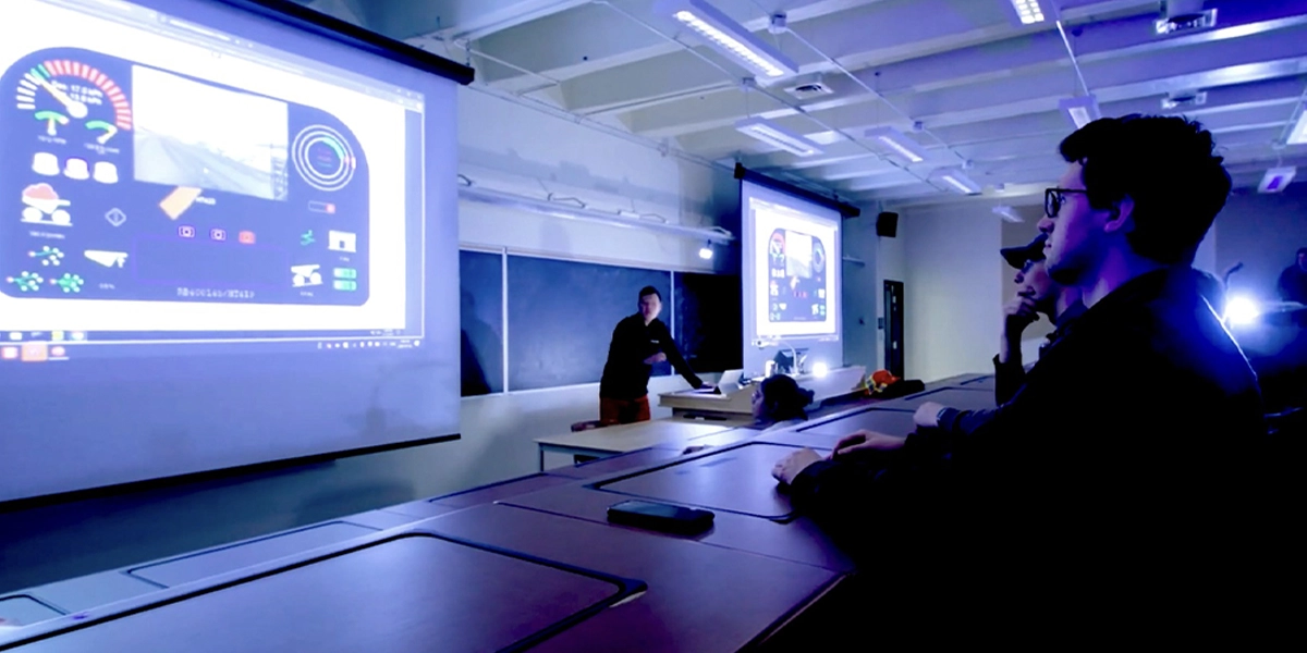 Students in a mechanical engineering class, looking at the image projected on the screen behind the professor.