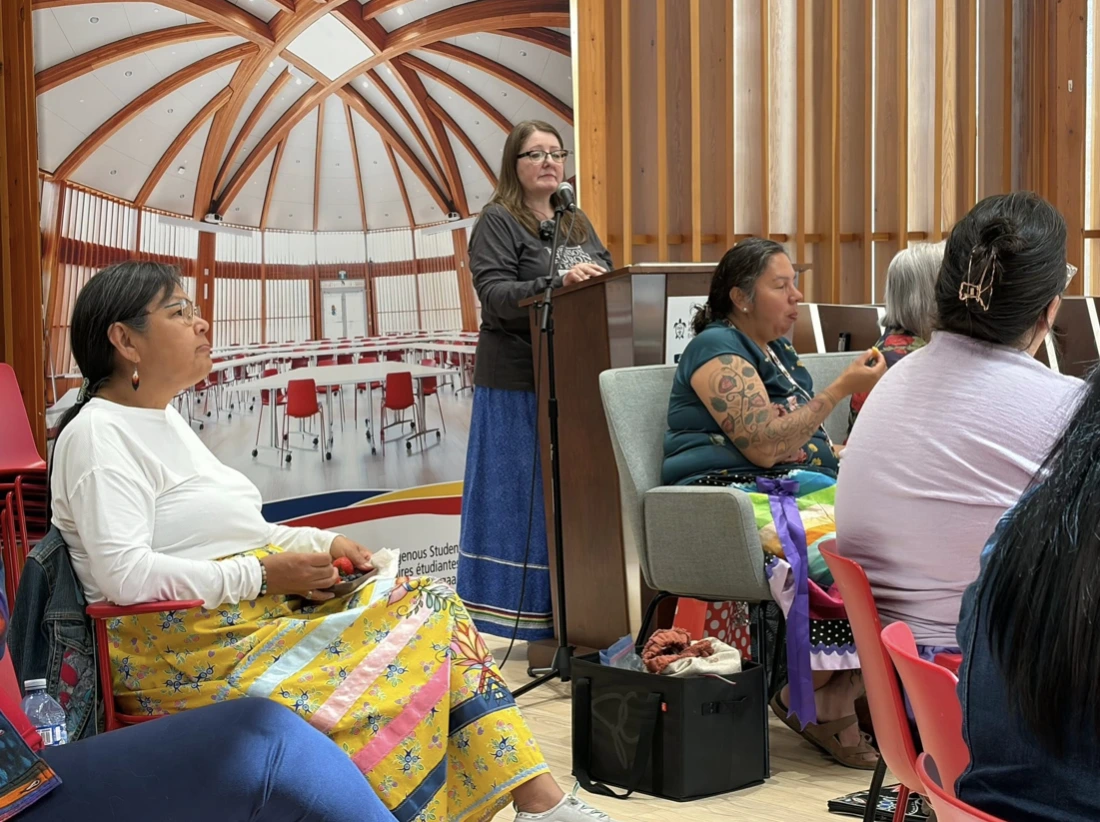 Pictured from left to right, Annette Cristo, Elizabeth Carlson-Manathara, and Lisa Osawamick gather during the June project launch event inside the Indigenous Sharing and Learning Centre at Laurentian University. Elizabeth presents at a podium while community and team members sit together in a circle.
