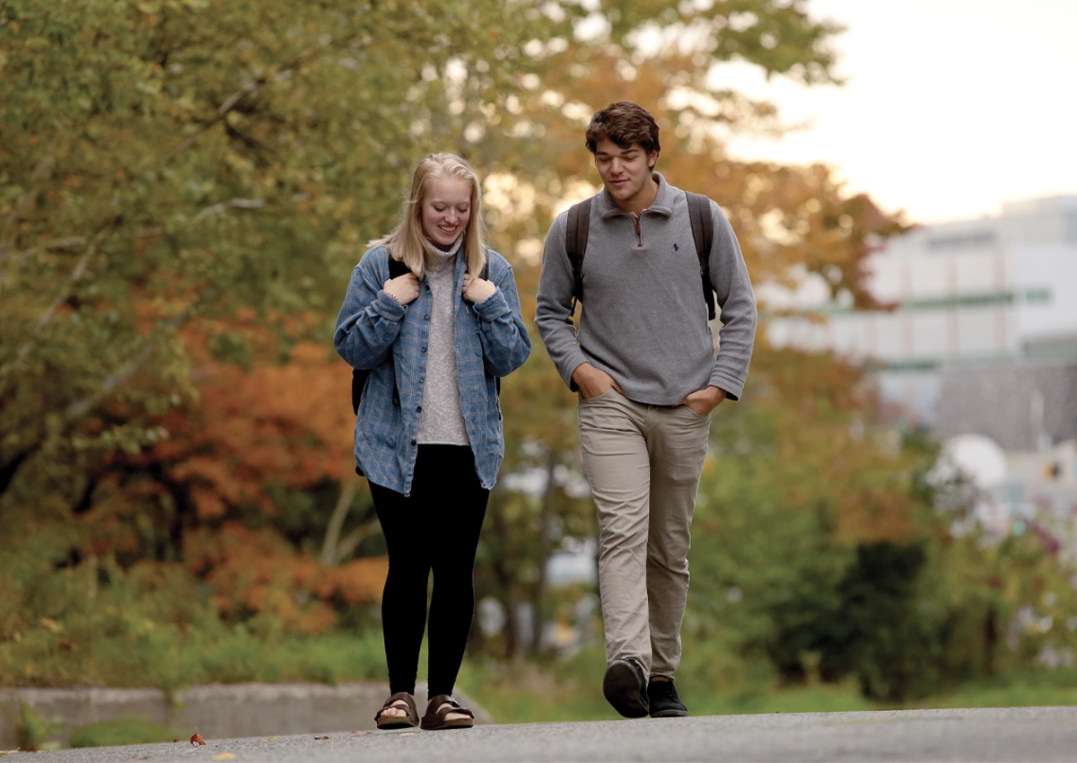 Students walking on campus with autumnal trees in the background.