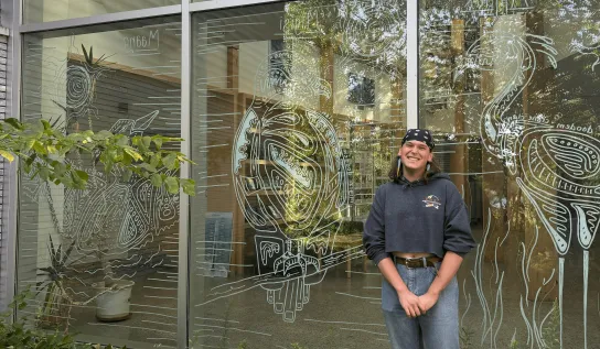 Person standing in front of a window with intricate white line art illustrations on the glass.