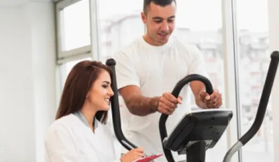 A man doing leg raises on a piece of equipment while being monitored and spoken to by a researcher.