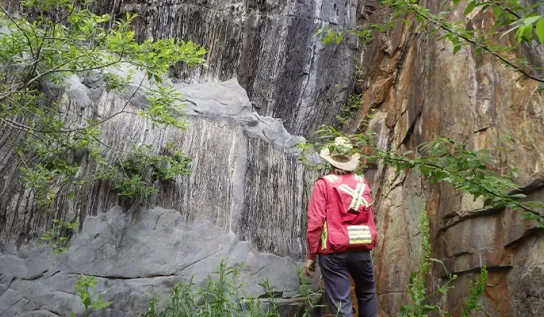 someone stands in front of a massive rock formation in high visibility gear