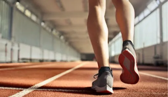A person shown from the thighs down running on a racetrack.
