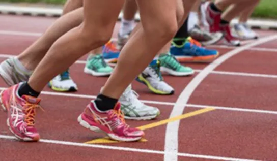 People shown from the thighs down lined up at the start of a racetrack.