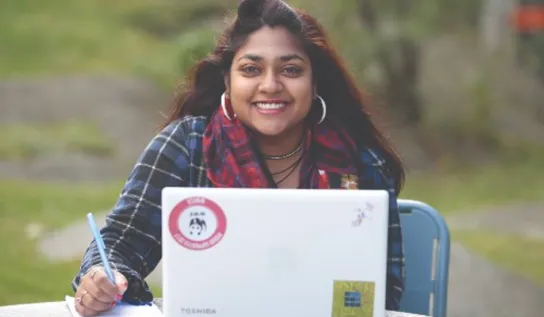 A female student with a laptop smiling.