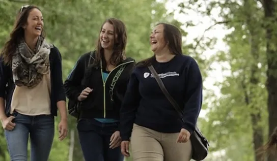 3 young women talking and smiling while walking along a tree-lined path.