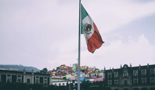 The flag of Mexico displayed above a city landscape.