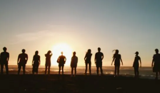 people stand on top of a hill with their backs to the camera while the sun sets
