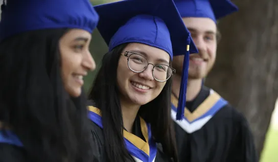 Three students wearing black, blue and yellow convocation attire, smiling.