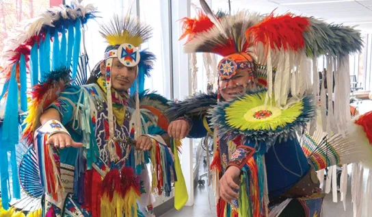 Two Indigenous Powwow dancers posing and smiling in their regalia.