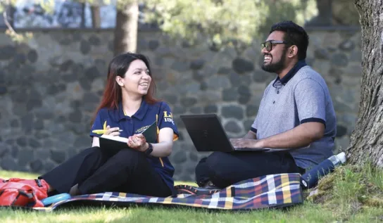 Two Laurentian University students studying on the grass outside.