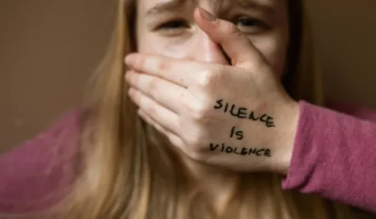 Woman covering her mouth, Silence is Violence written on her hand