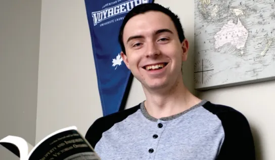 A Laurentian University student reading a book in his dorm room.