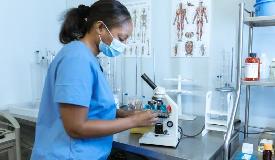 A student is wearing mask while looking at a microscope specimen