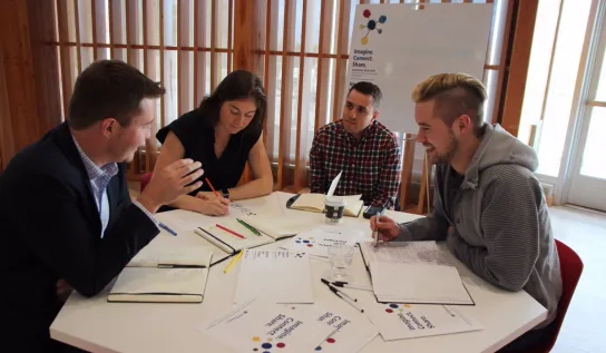 Four people are filling out paper work around a table