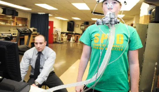 A researcher on a computer and a woman with respiration monitoring equipment on her face.